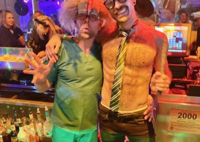 Two employees dressed in costumes behind Dunes Resorts' bar for Halloween 2021 Party