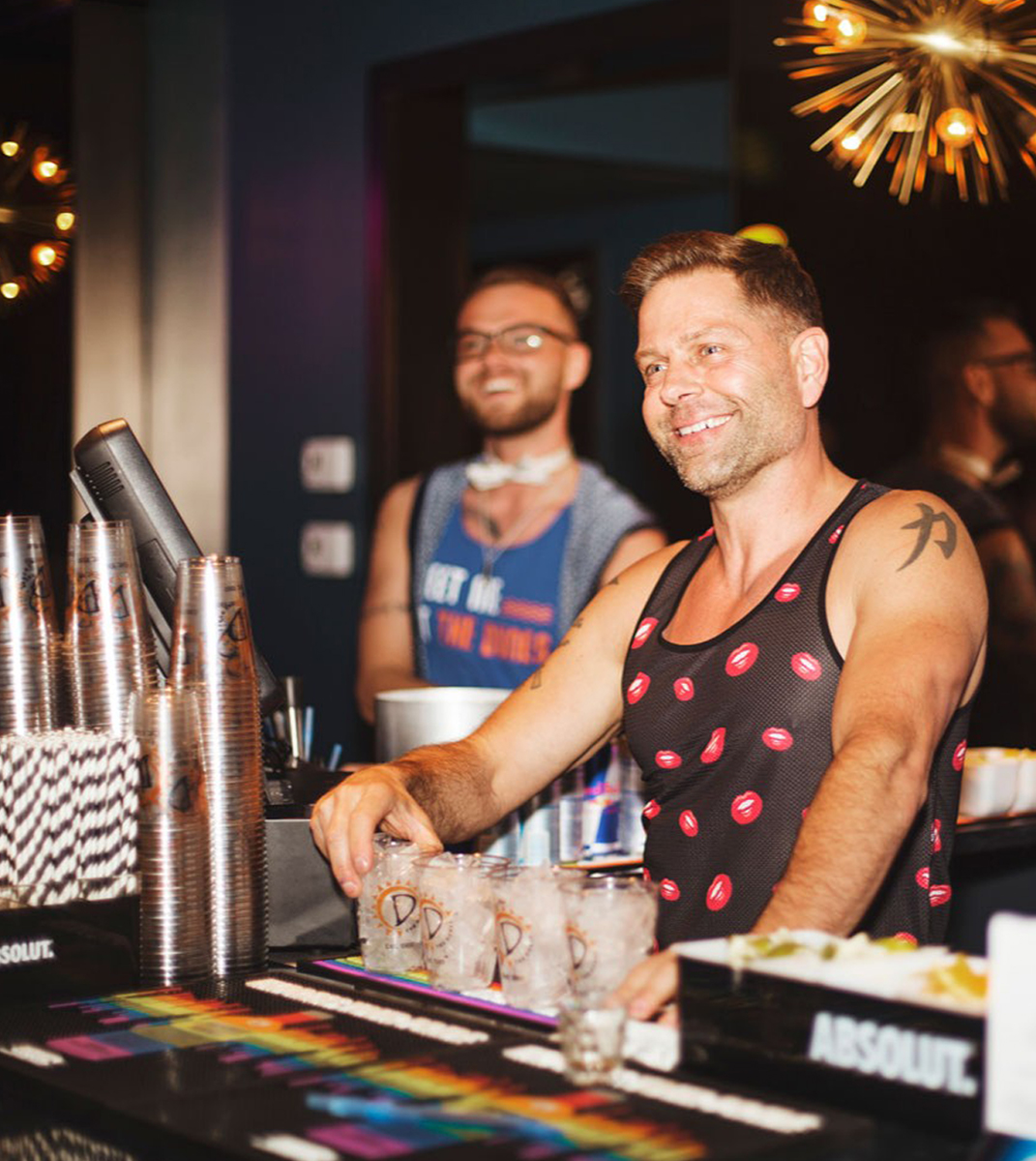 A Dunes Resort worker stands behind the bar making drinks and smiling at guests.