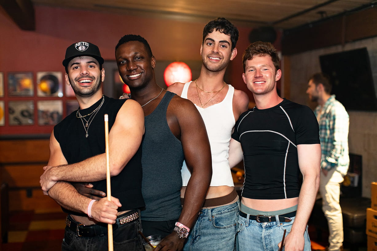 Four people in tank tops and summery outfits pose in the Vinyl Lounge with a pool cue.