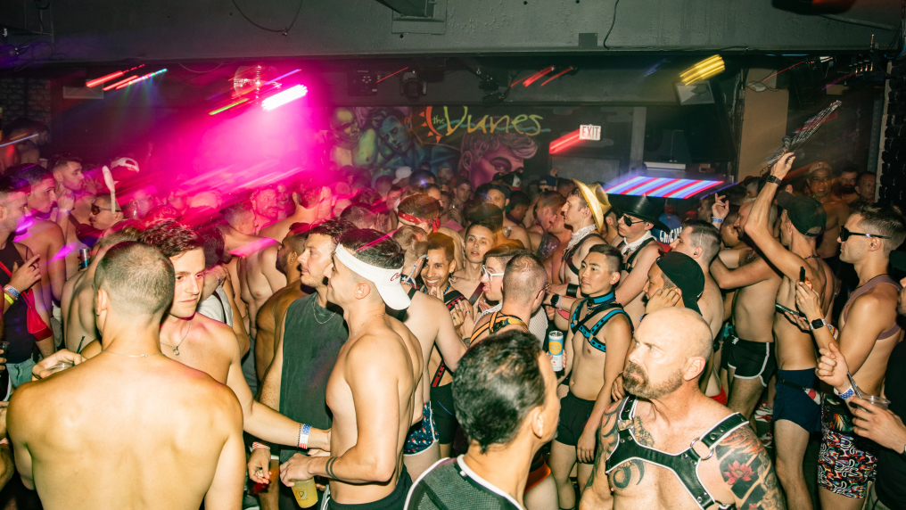 A vibrant nightclub scene with a lively crowd of shirtless men dancing, wearing various outfits and accessories