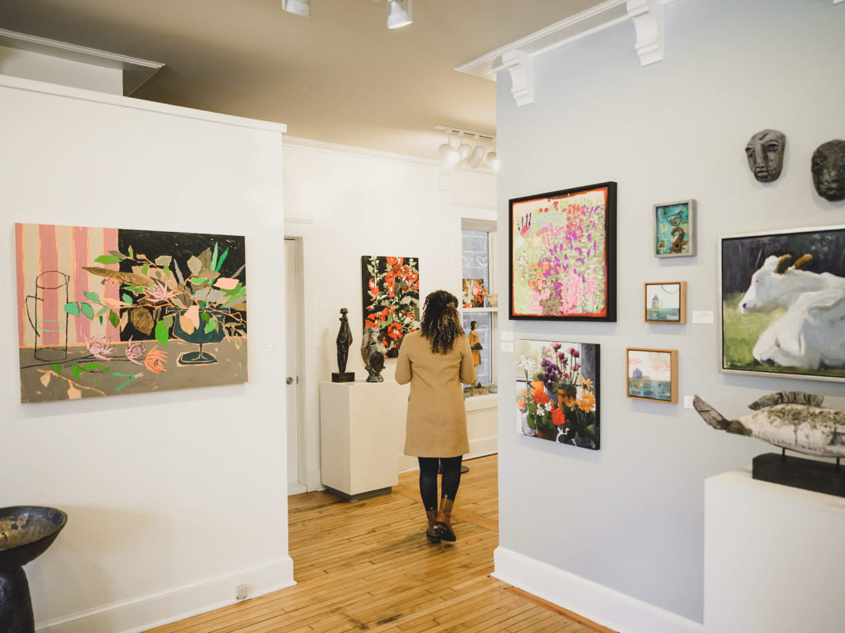 A visitor explores vibrant art in a cozy gallery in the Saugatuck/Douglas area, surrounded by colorful paintings and sculptures.