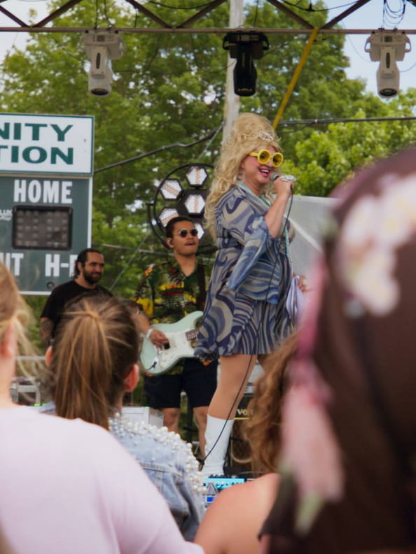 A lively outdoor concert at the Saugatuck Center for the Arts features a vibrant performer in colorful attire, engaging the crowd.