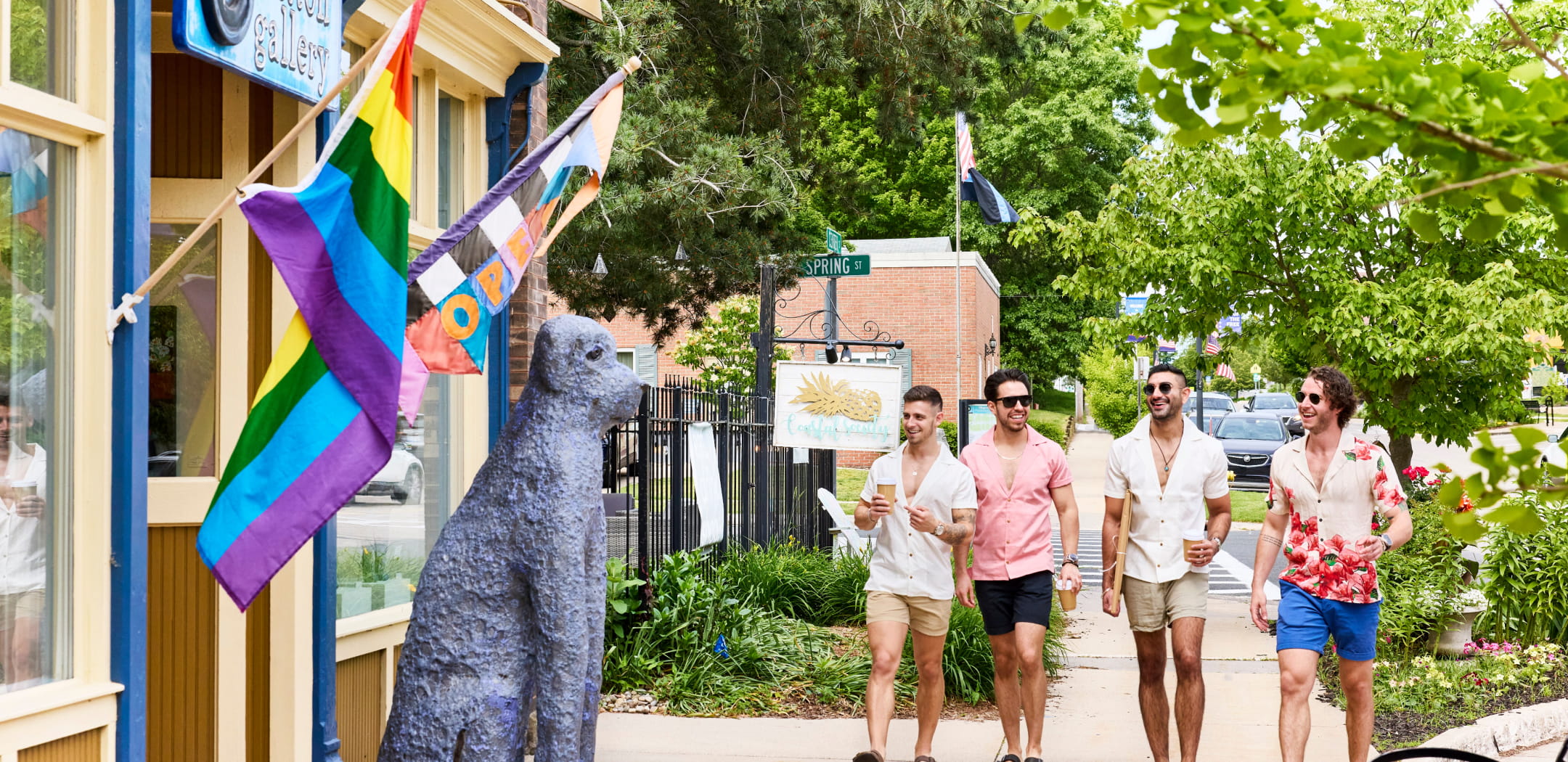 Four friends stroll past a colorful gallery and flags in downtown Saugatuck, enjoying a sunny day.
