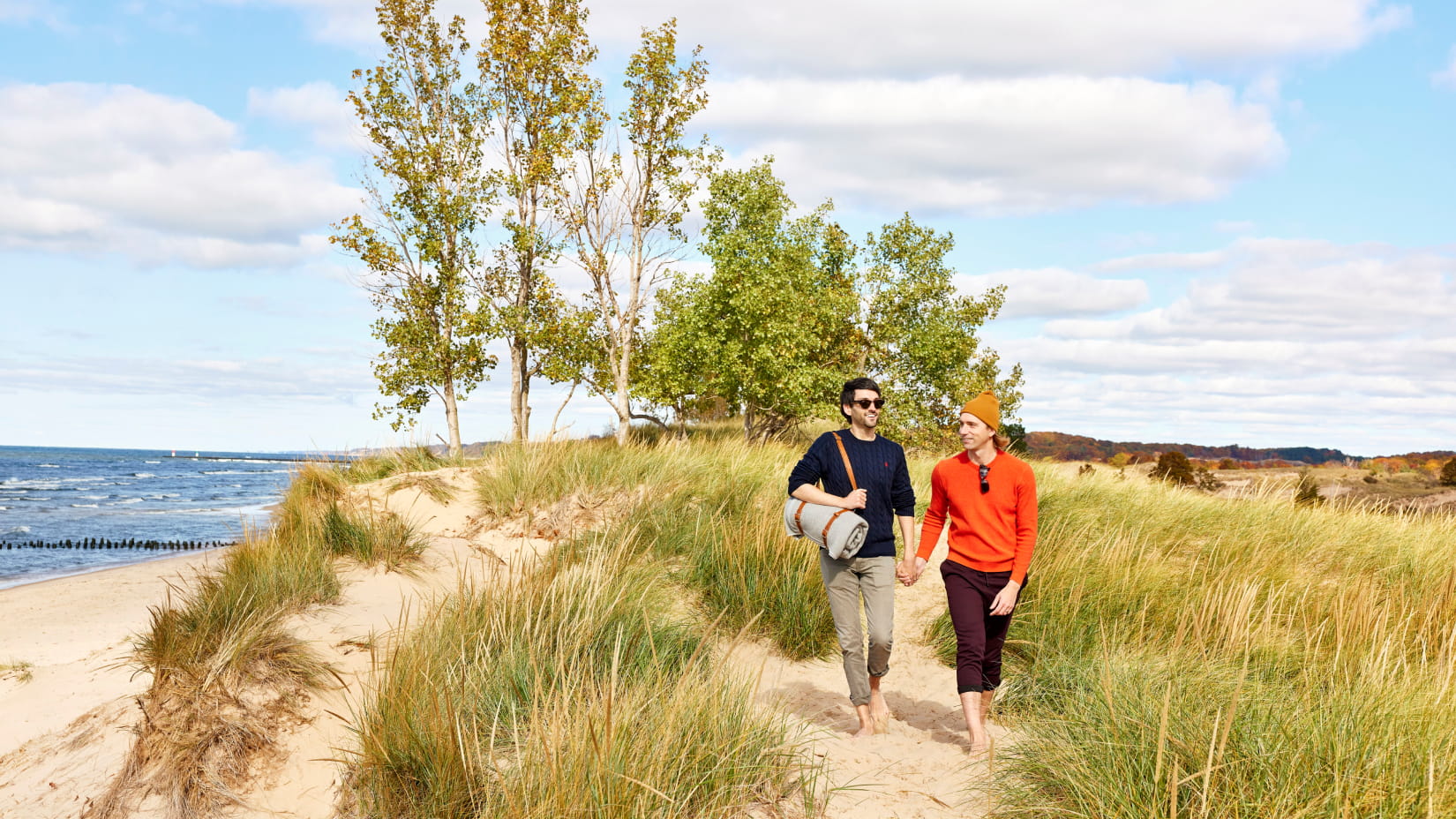 Couple walks barefoot on a sandy dune path, with Lake Michigan waves in the background.
