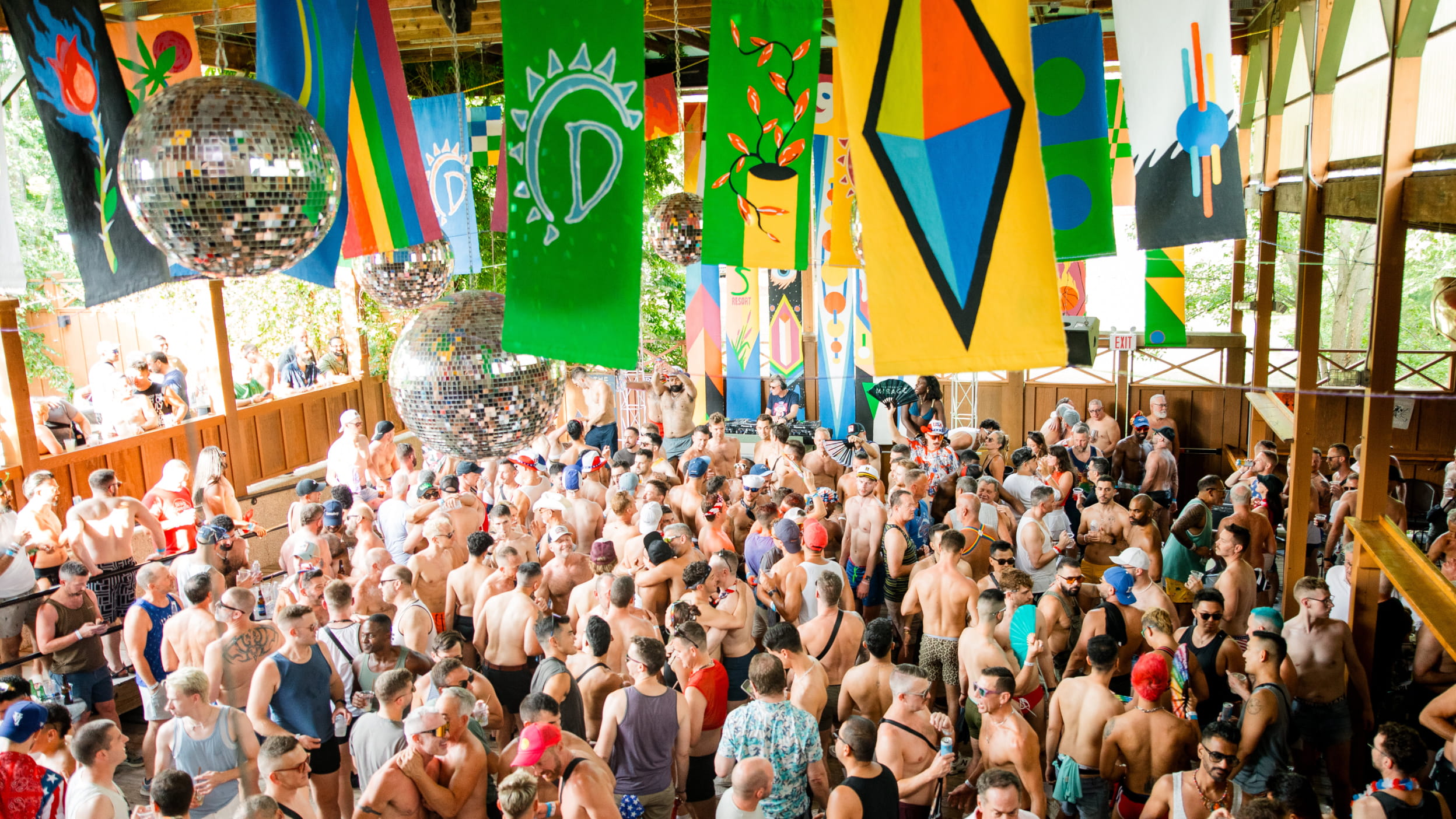 A lively crowd dances on the Deck under colorful banners and disco balls, enjoying a Tea Dance.